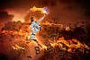 Image of a businesswoman with a fire jumping high against flaming background