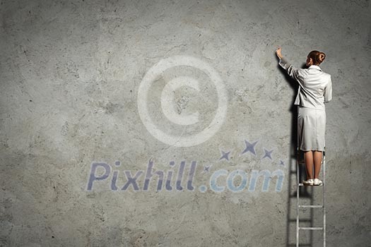 Businesswoman standing on ladder drawing diagrams and graphs on wall