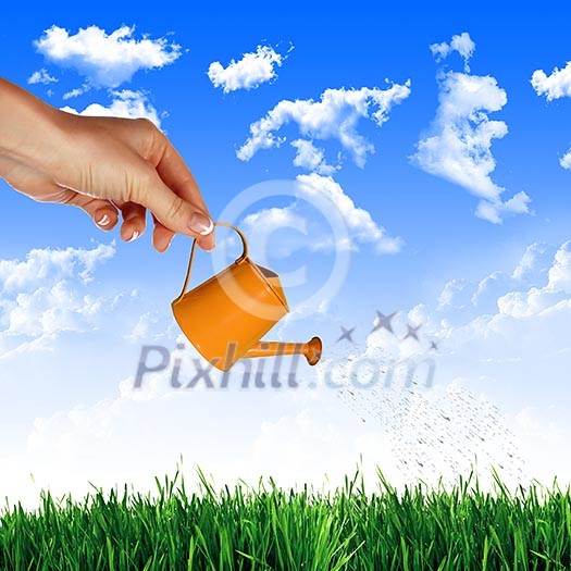 Hand with a small watering can watering green grass Hand with a small watering can watering green grass