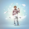Image of little boy playing with paper airplane against blue background