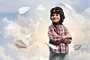 Image of little boy in pilots helmet with paper airplanes in background