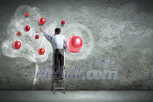 Businessman on ladder pointing at illustrated apple tree