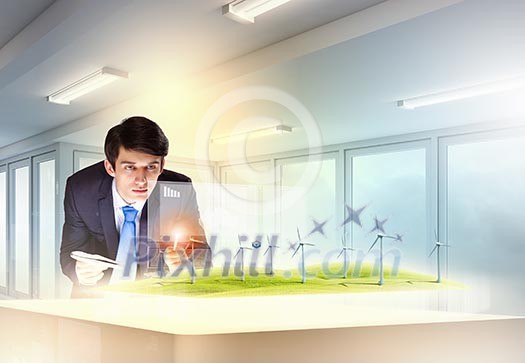 Image of young businessman looking at high-tech picture of windmills Image of young businessman looking at high-tech picture of windmills