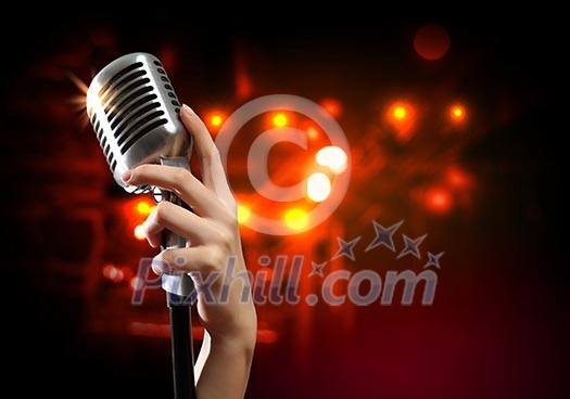 Female hand holding a single retro microphone against colourful background Female hand holding a single retro microphone against colourful background