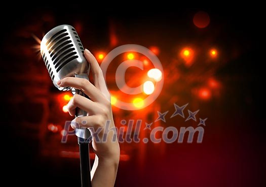 Female hand holding a single retro microphone against colourful background