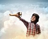 Image of little boy in pilots helmet playing with toy airplane against clouds background