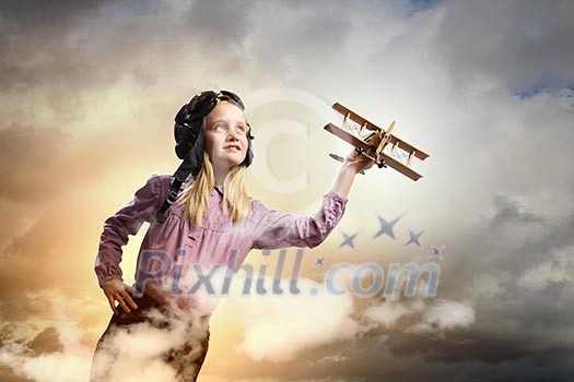 Image of little girl in pilots helmet playing with toy airplane against clouds background