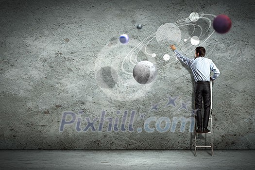 Image of businessman drawing planets on wall