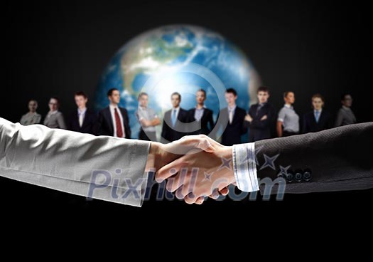 business handshake against black background and standing businesspeople