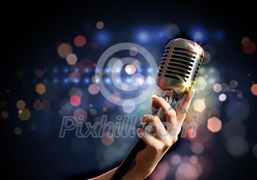 Female hand holding a single retro microphone against colourful background Female hand holding a single retro microphone against colourful background