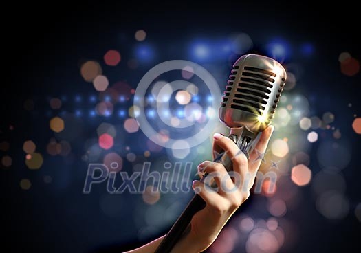 Female hand holding a single retro microphone against colourful background