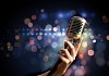 Female hand holding a single retro microphone against colourful background