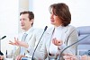 Image of two businesspeople sitting at table at conference speaking in microphone