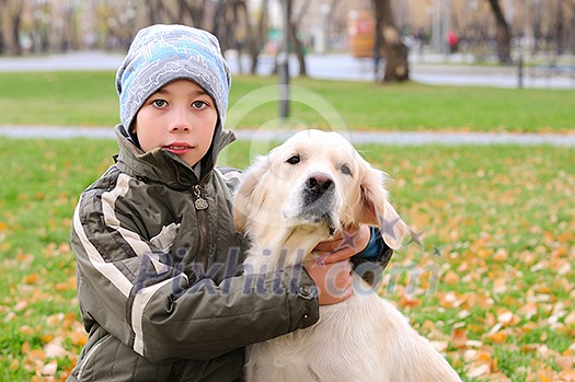 Boy playing in autumn park with a golden retriever.