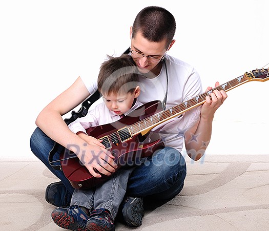 A young father teaches his young son to play guitar