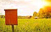 A postbox, mailbox with a house in the background and a sunset in summer. Green field