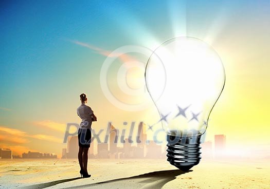 Image of businesswoman looking at light bulb. Green energy concept