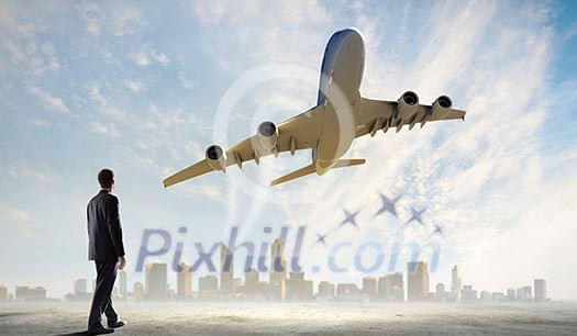 Image of businessman standing with back looking at airplane in sky Image of businessman standing with back looking at airplane in sky
