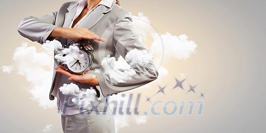 Image of young businesswoman holding alarmclock against cloudy background