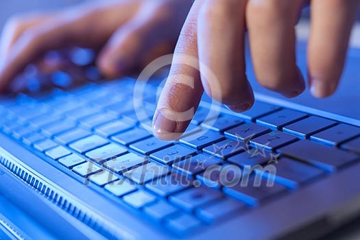 Click! Hands of a man on a keyboard with blue backlighting.