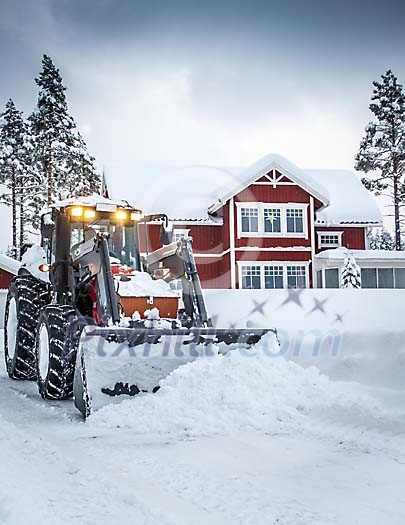 A red tractor plowing snow in front of a red house