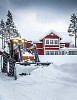 A red tractor plowing snow in front of a red house