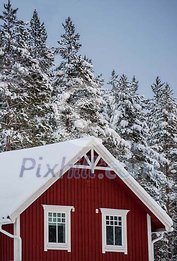 A red wooden hose with snow on the roof and snowy trees A red wooden hose with snow on the roof and snowy trees