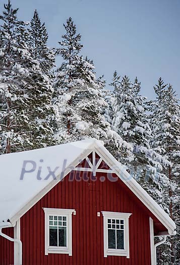 A red wooden hose with snow on the roof and snowy trees