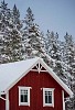 A red wooden hose with snow on the roof and snowy trees