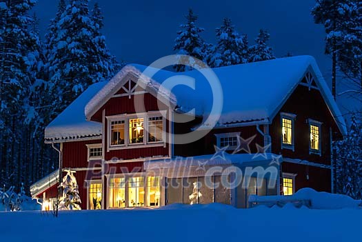 A red wooden house covered with snow. Christmas lights in tree