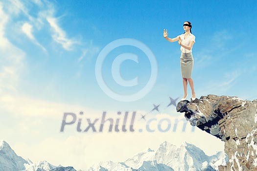 Image of businesswoman in blindfold standing on edge of mountain