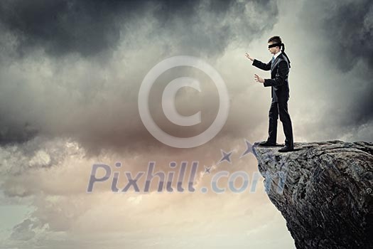 Image of businessman in blindfold standing on edge of mountain