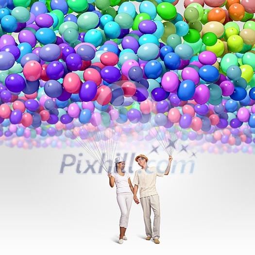 Image of young couple holding bunch of colorful balloons