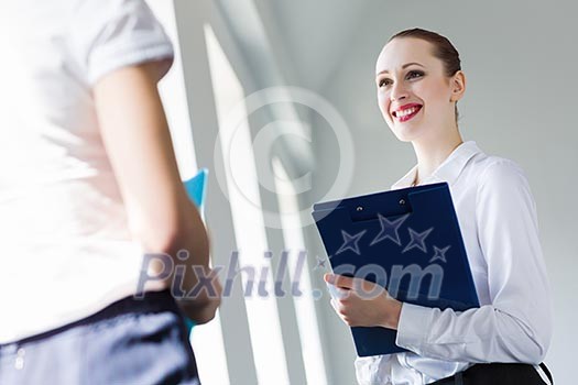 Image of young businesswoman holding folder and talking to colleague