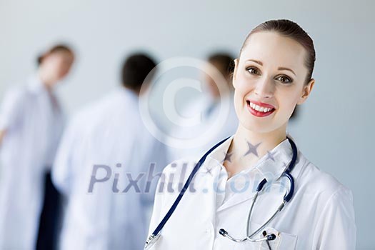 Attractive female doctor in white uniform with colleagues at background Attractive female doctor in white uniform with colleagues at background