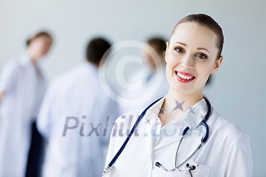 Attractive female doctor in white uniform with colleagues at background