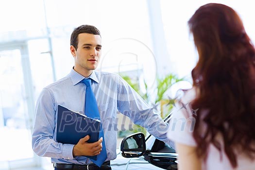 Attractive woman at car salon with consultant choosing a car