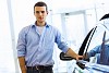 Handsome young man consultant at car salon standing near car