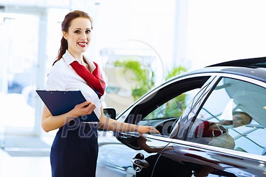 Young attractive woman consultant of car center standing near car Young attractive woman consultant of car center standing near car