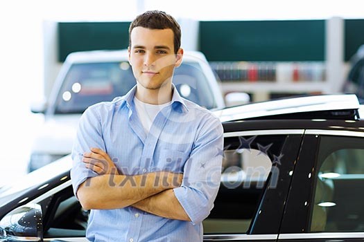 Handsome young man consultant at car salon standing near car Handsome young man consultant at car salon standing near car