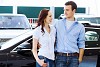 Two pretty young people smiling standing near car