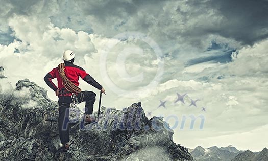 Image of young man mountaineer standing atop of rock