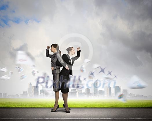 Image of two businesswomen looking into distance standing back to back Image of two businesswomen looking into distance standing back to back