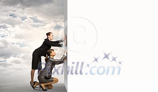 Image of two businesswomen pushing blank wall. Place for text