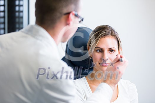 Optometry concept - pretty young woman having her eyes examined by an eye doctor (shallow DOF; color toned image)