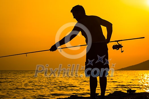 Fisherman silhouette on the beach at colorful sunset