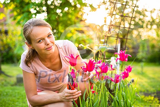 Pretty female gardener taking care of her lovely garden on a spring day - admiring the tulips