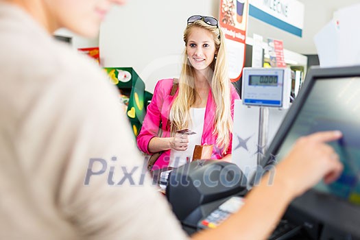 Beautiful young woman paying for her groceries at the counter of a grocery store/supermarket (color toned image) Beautiful young woman paying for her groceries at the counter of a grocery store/supermarket (color toned image)