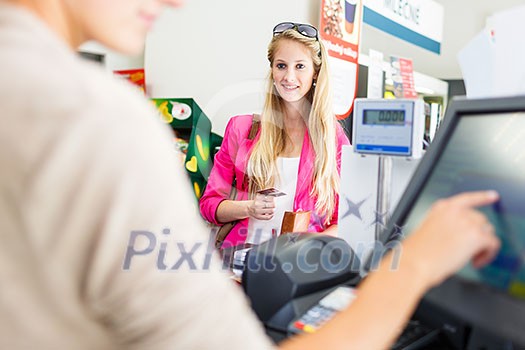 Beautiful young woman paying for her groceries at the counter of a grocery store/supermarket (color toned image)