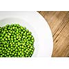 Healthy and lovely green peas in a plate on a wooden table (color toned image)